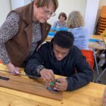 4 personnes (enfants et adultes) autour des tables confectionnent les éléments pour le corso fleuri