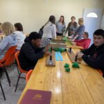12 personnes (enfants et adultes) autour des tables confectionnent les éléments pour le corso fleuri