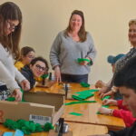 9 personnes (enfants et adultes) autour des tables confectionnent les éléments pour le corso fleuri