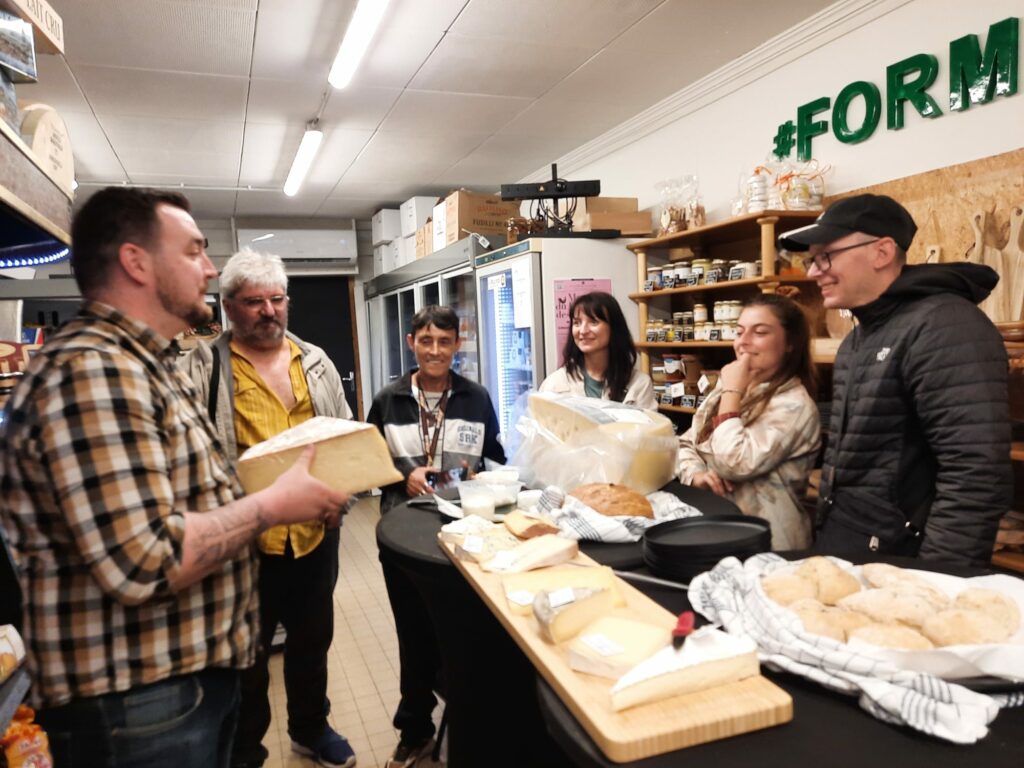 Dans l'épicerie de Marc, professionnels et personnes accompagnées du SAMSAH dégustent les fromages avec le patron de l'épicerie