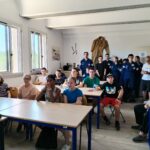 Le groupe, dans une salle type "classe" écoute les explications du référent militaire