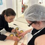 Elona et une jeune fille déposent la pâte dans les moules à tartes