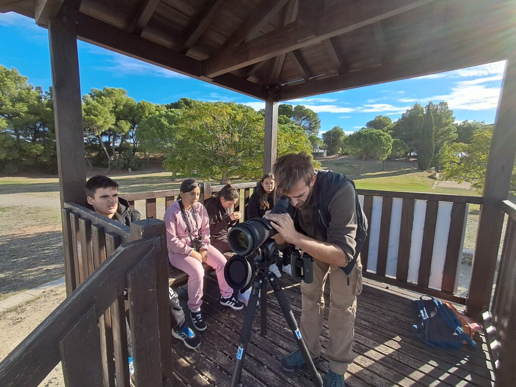 L'animateur regarde dans le grand objectif d'un appareil photo. A ces côtés 4 jeunes le regardent