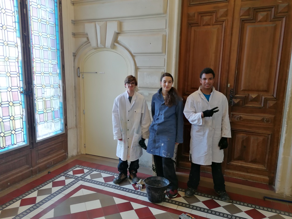 3 jeunes posent devant la porte peinte du château