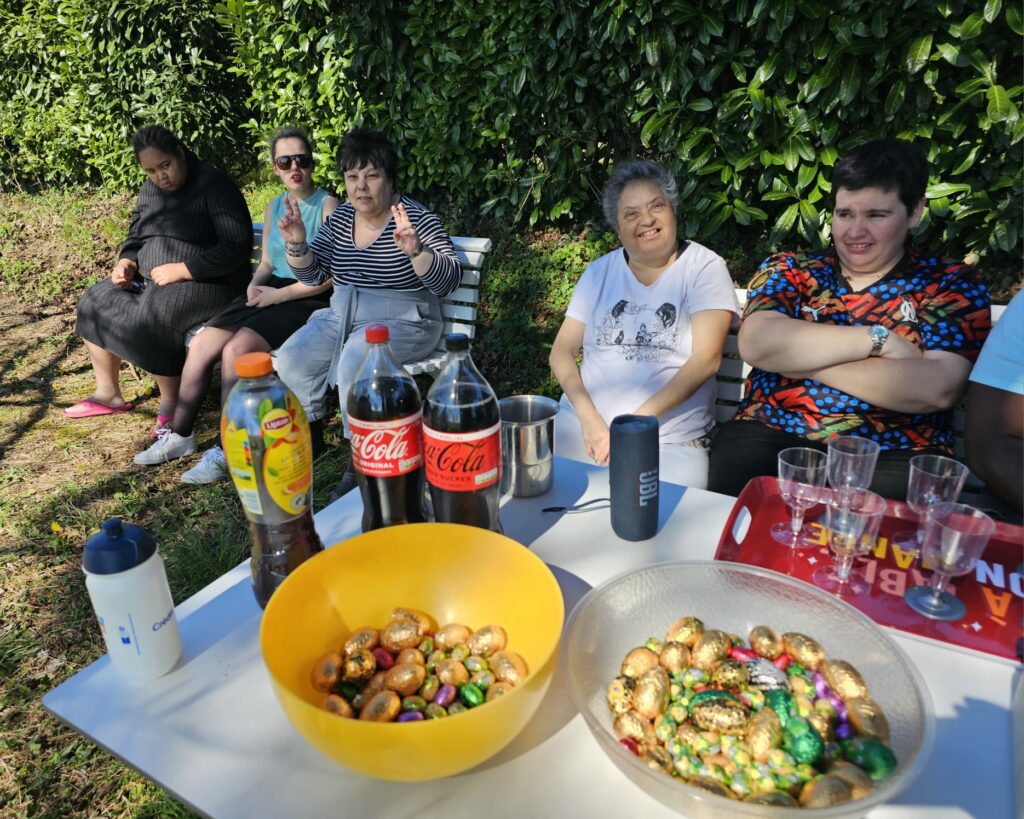 Des résidents assis dans le jardin derrière une table remplie de chocolats de pâques et de boissons rafraichissantes