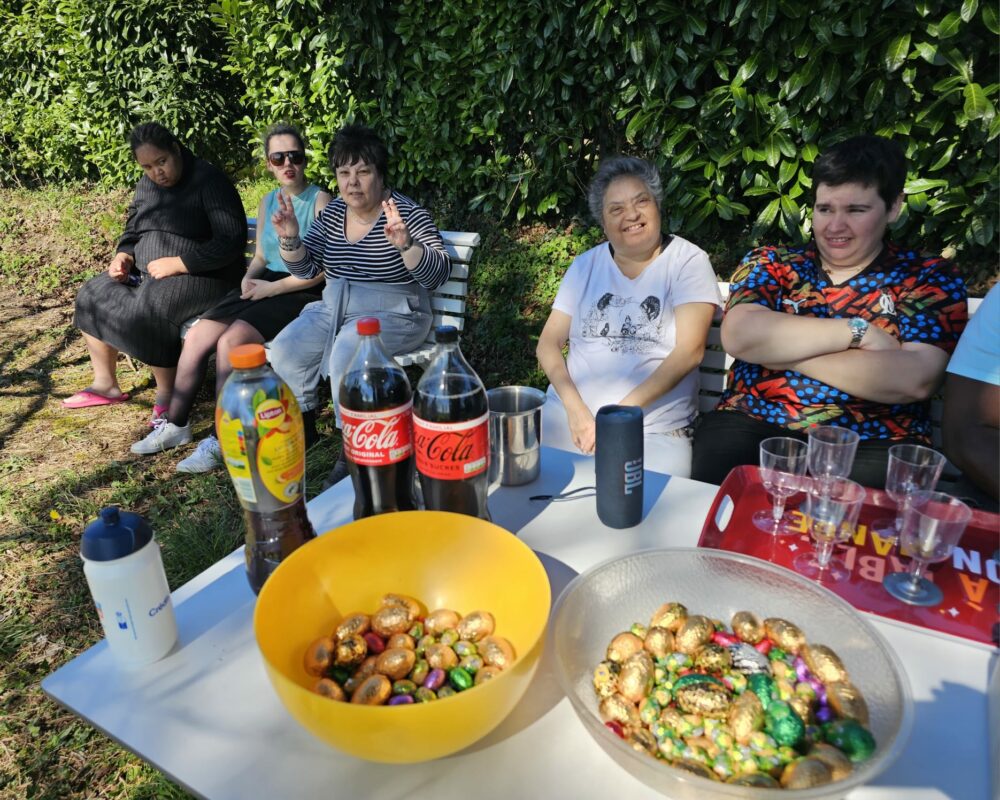 Des résidents assis dans le jardin derrière une table remplie de chocolats de pâques et de boissons rafraichissantes